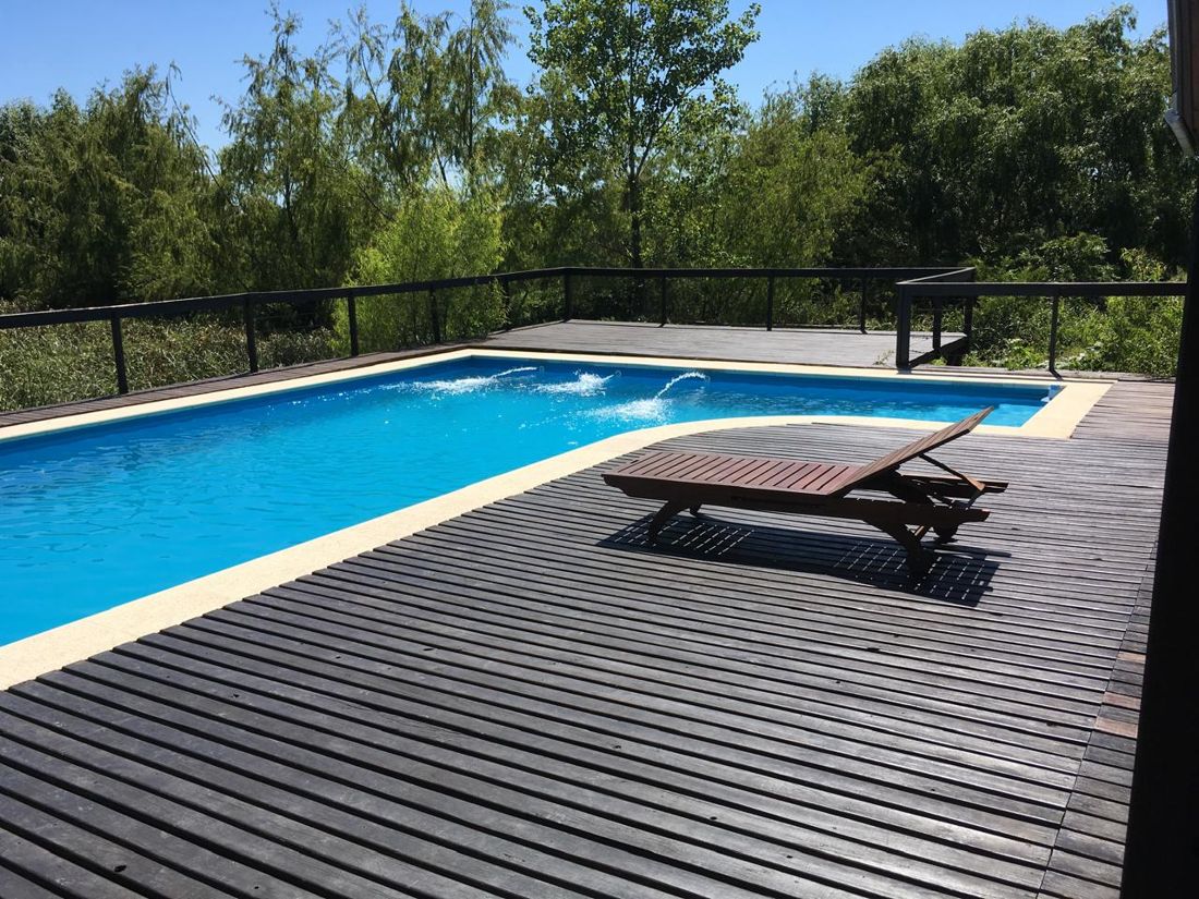 Pileta con deck de madera y reposera, rodeada de monte
